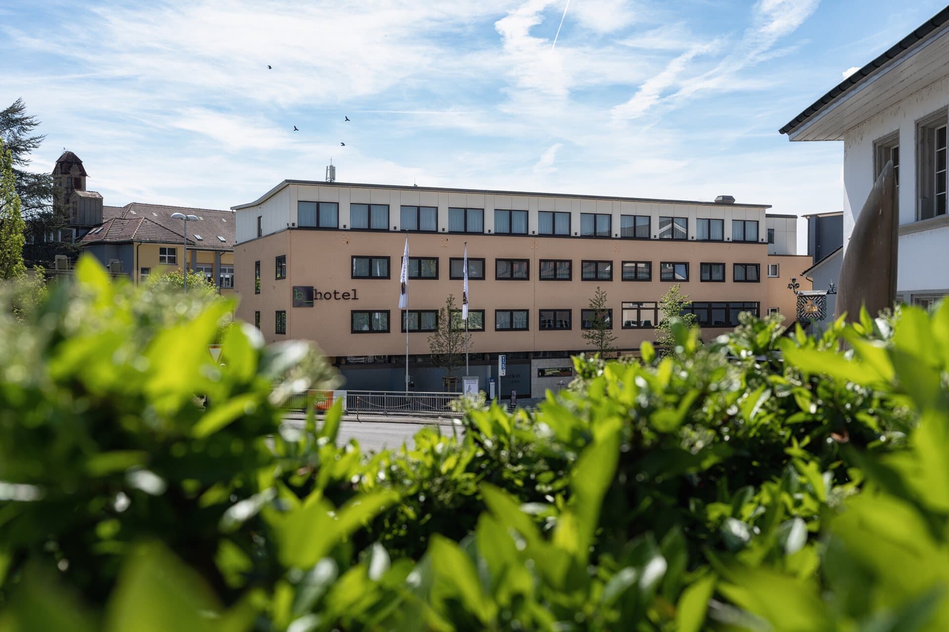 View of the b smart Hotel in Schonenwerd with a modern four story building in the background and green plants in the foreground