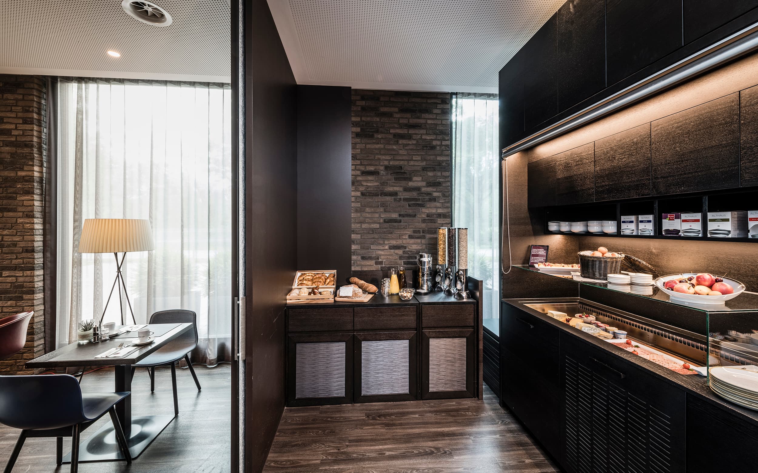 A breakfast room in the B_smart Hotel in Bendern with a set table, baked goods, cereal, and a fresh fruit buffet.