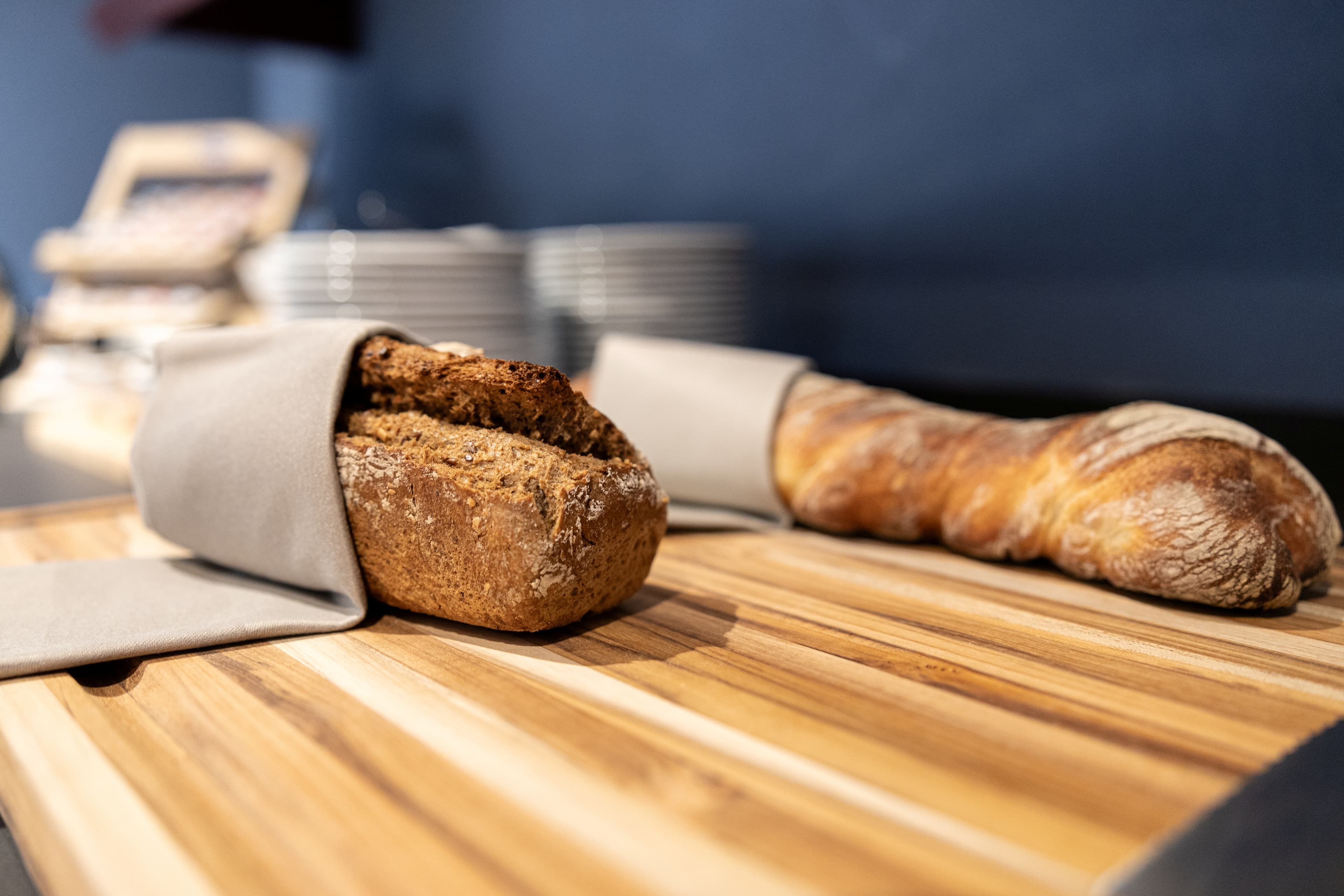 Two different types of bread wrapped in linen cloths are lying on a wooden cutting board in the breakfast area of the B Smart Hotel Arbon