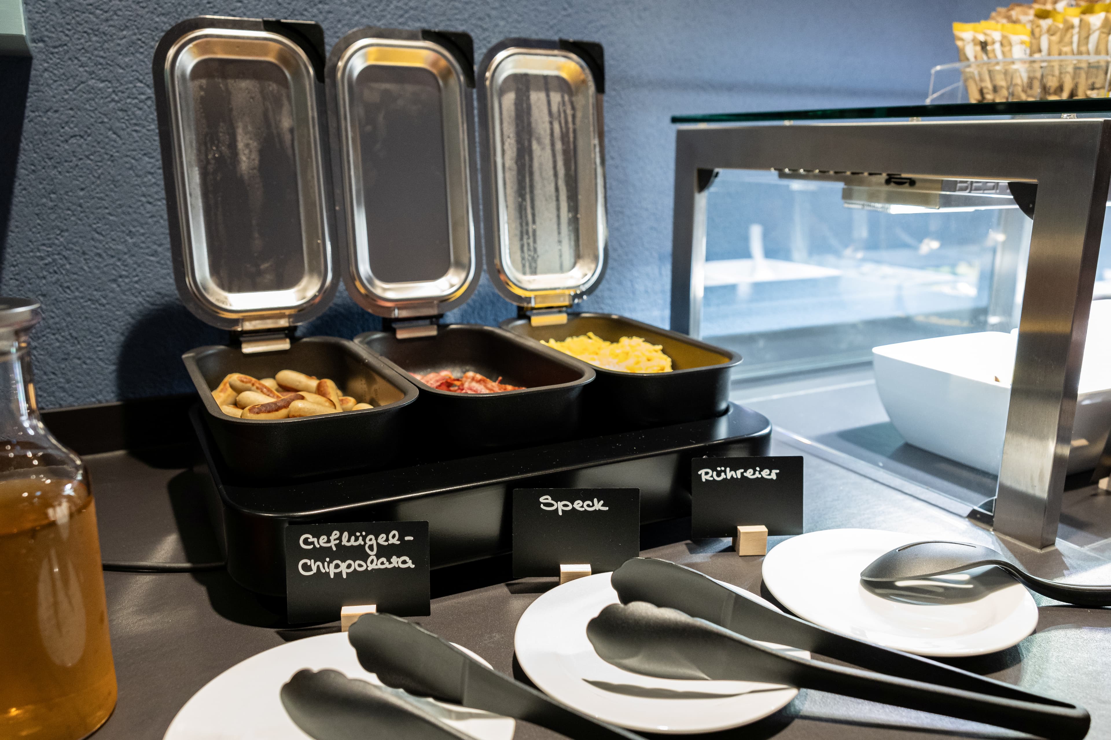 Breakfast buffet at the B Smart Hotel Arbon with poultry chipolata, bacon, and scrambled eggs in chafing dishes