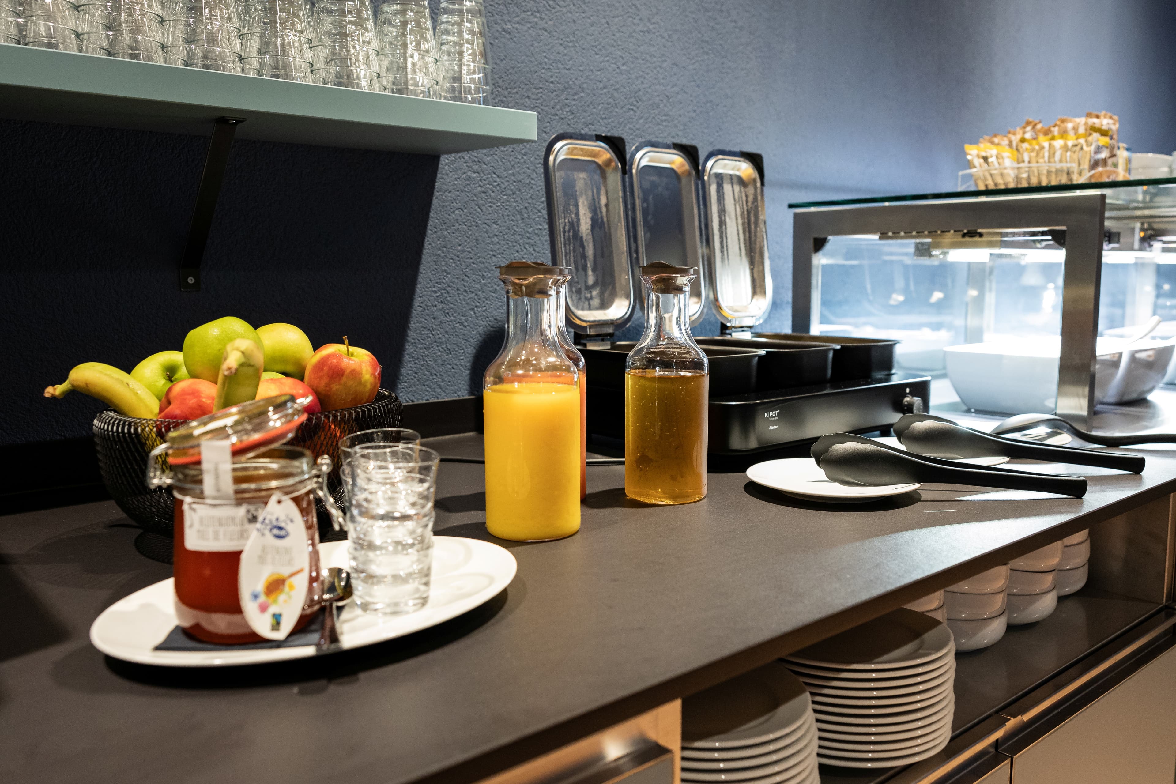 Breakfast buffet at B Smart Hotel Arbon with fresh fruit, juices, jam, and dishes on a counter.