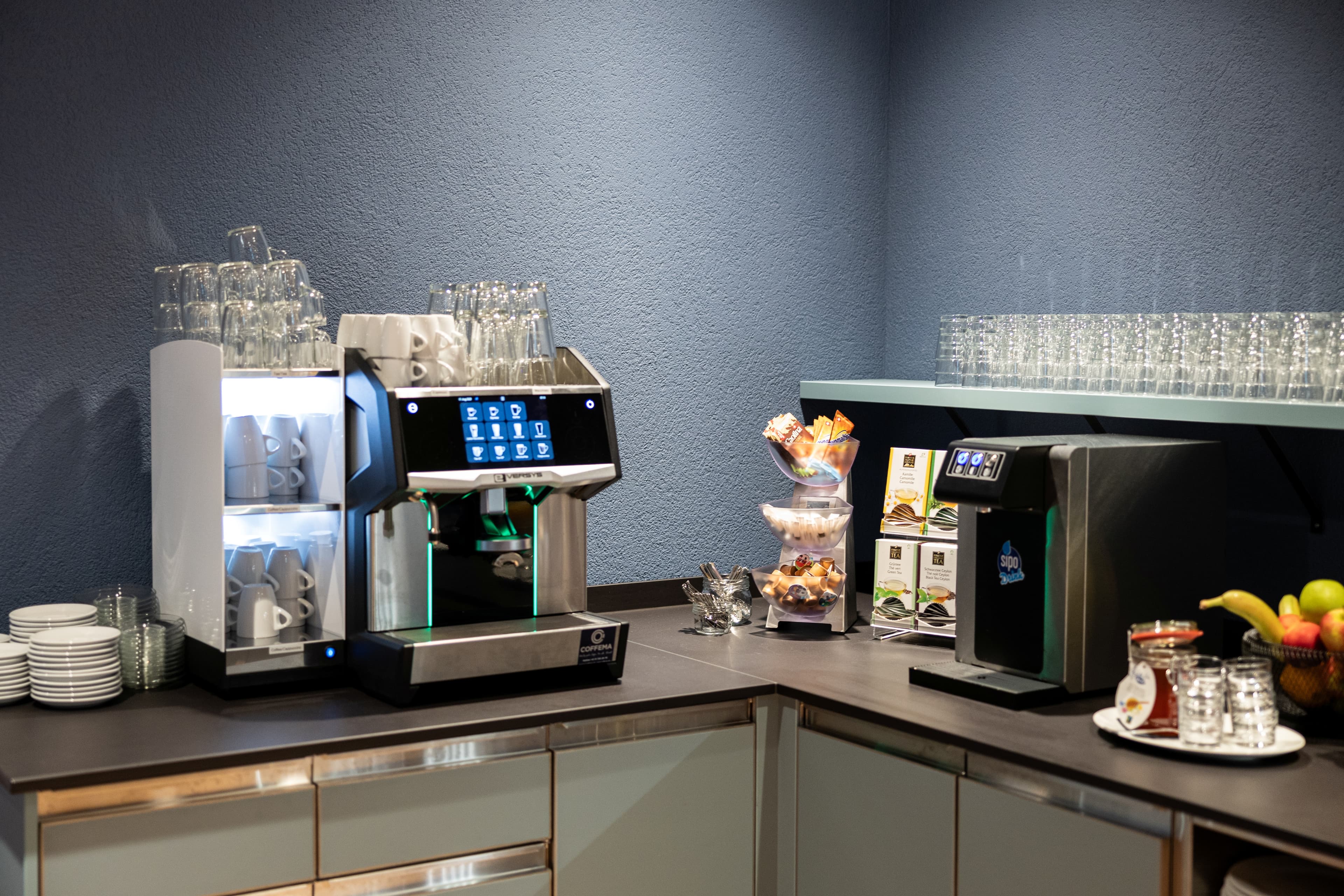 A breakfast room in the B_smart Hotel Arbon with a coffee machine, dishes, snacks, glasses, and a bowl of fruit.