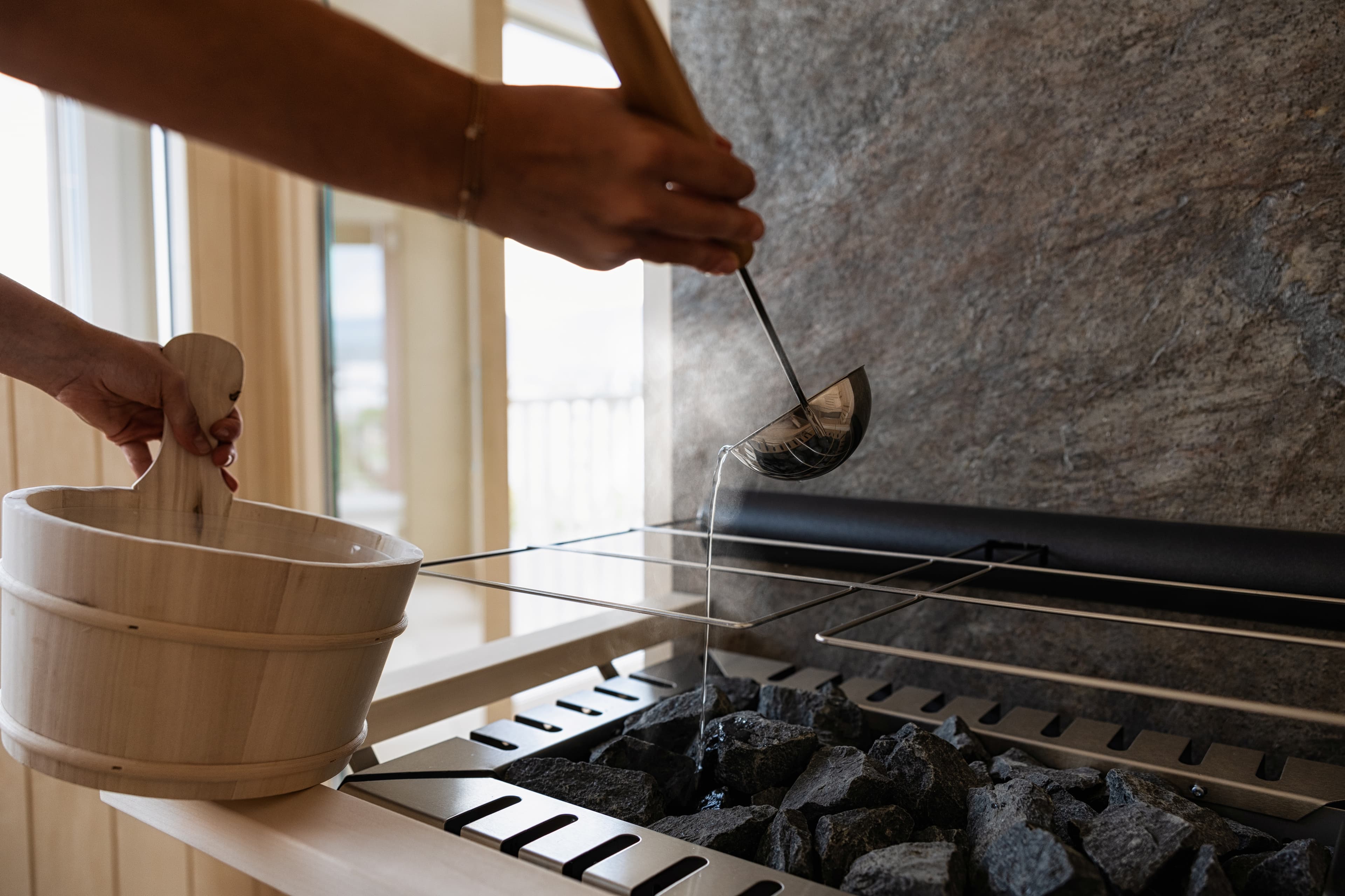 A person pours water with a ladle onto hot sauna stones at the B Smart Hotel Arbon.