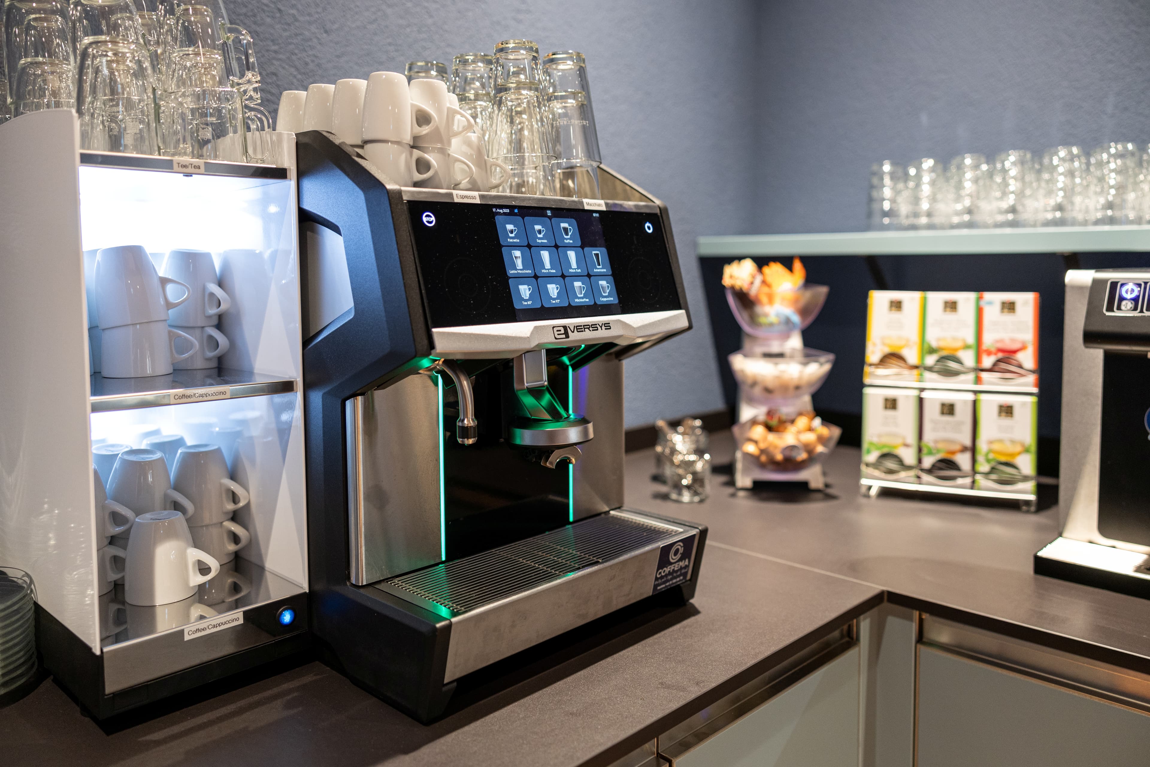 A modern coffee machine in a breakfast area of the B Smart Hotel Arbon surrounded by cups tea bags and snacks.