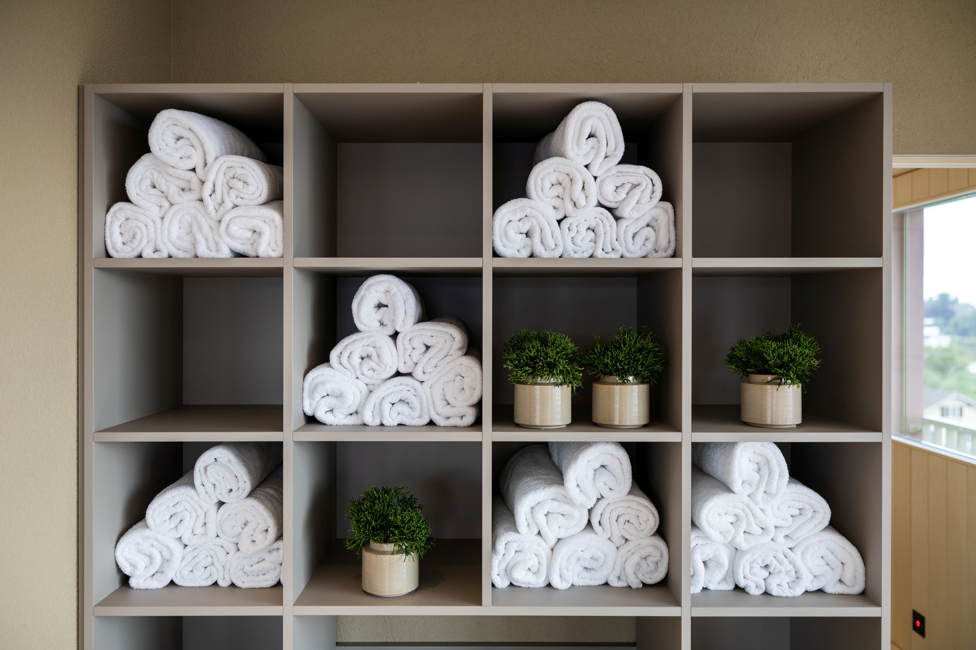 In a shelf at the B Smart Hotel Arbon, neatly rolled white towels and several small green plants in pots are lined up.