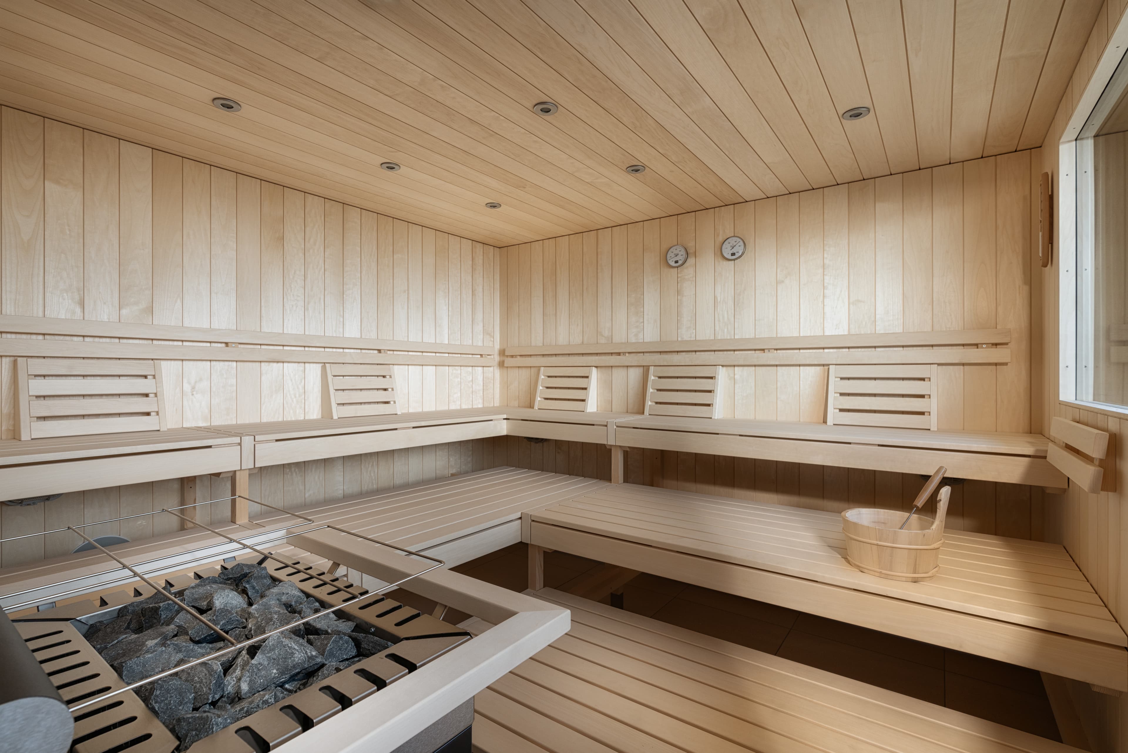 Interior view of a wood-paneled sauna in the Bsmart Hotel Arbon with benches a sauna stove and a bucket with a ladle