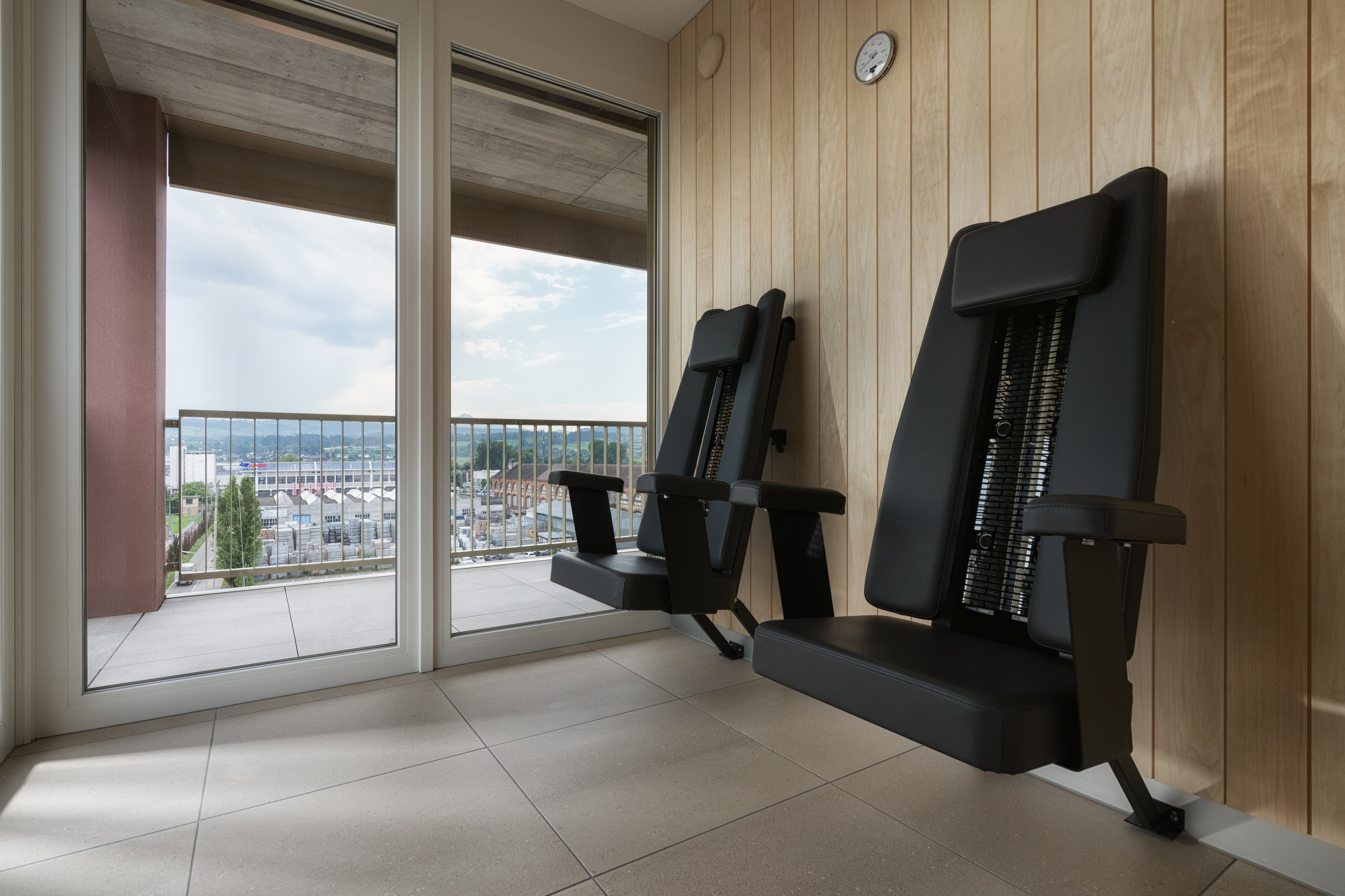 Two ergonomic chairs are in a room with wooden walls and a large window overlooking the city at the B Smart Hotel Arbon.