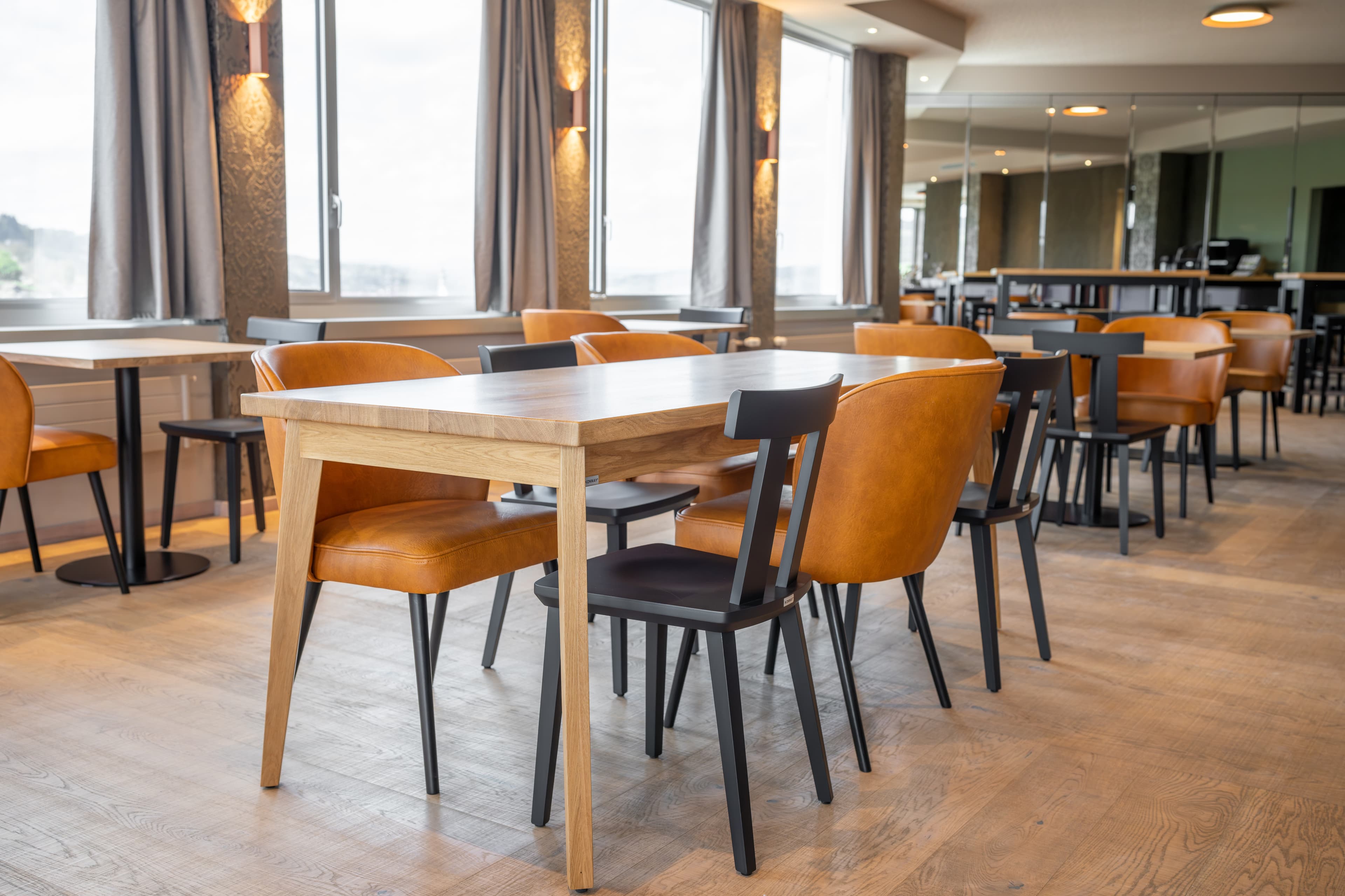 Modern breakfast room at the B_Smart Hotel Menziken with wooden tables and leather upholstered chairs in a warm color shade