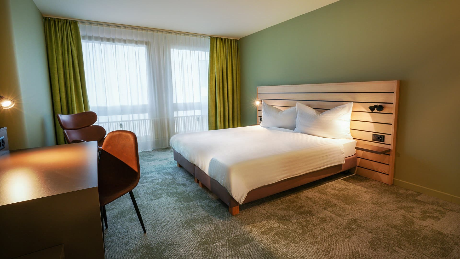 A modern hotel room at the Flexy Motel Buchs with a double bed desk and chair green walls and curtains
