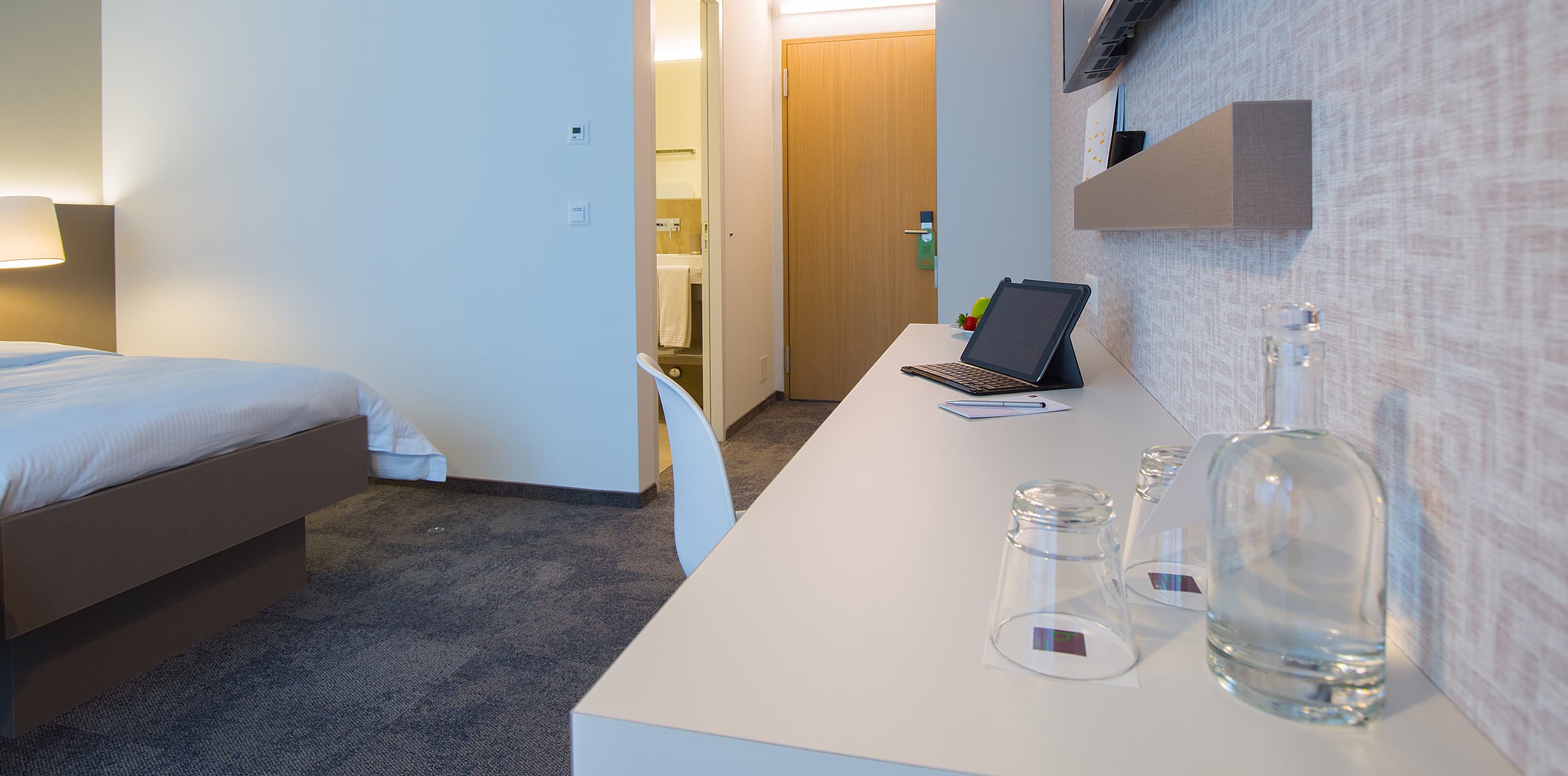 A modern double room at the B Smart Motel Landquart with a desk on which a tablet and two glasses are placed