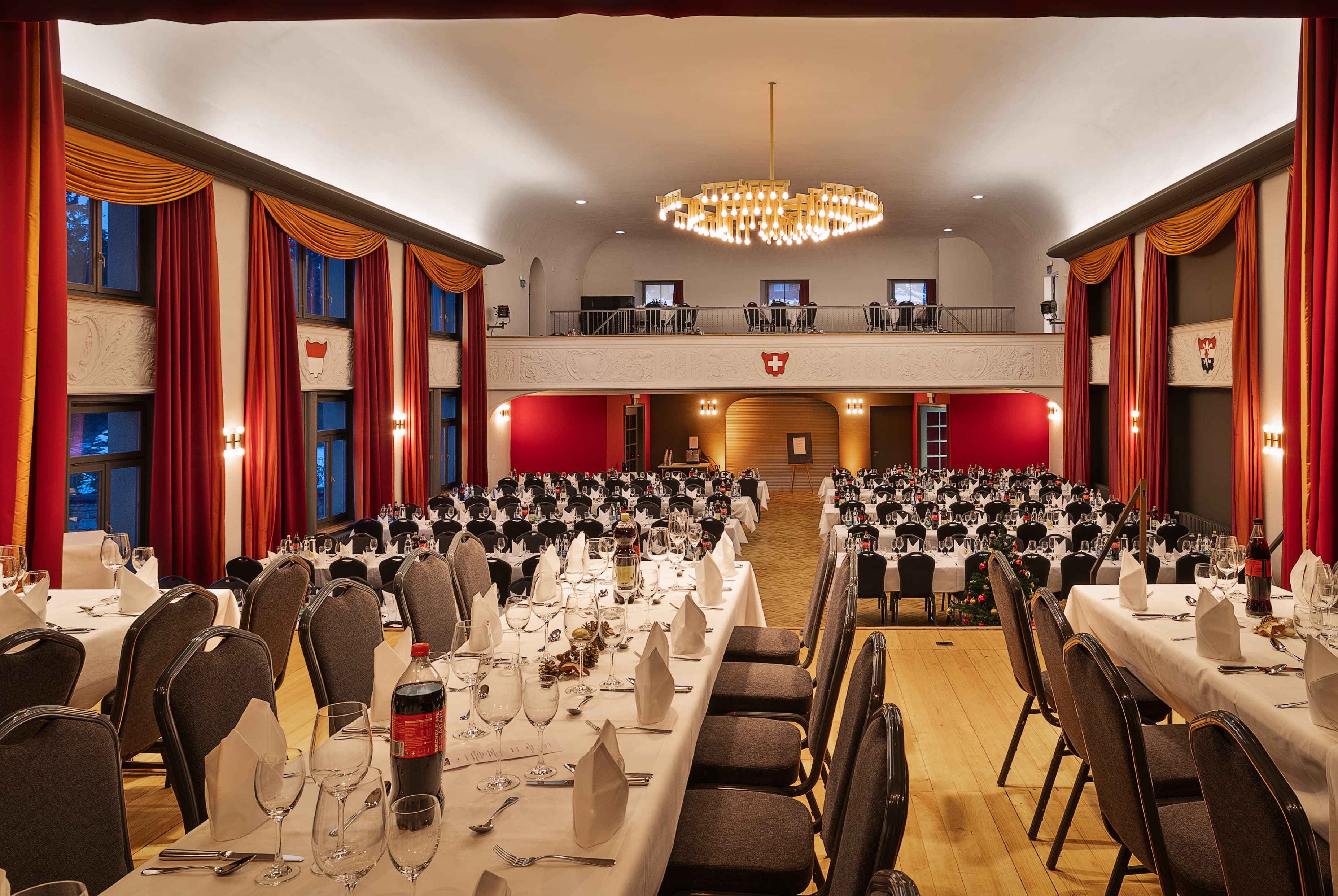 Festively decorated casino hall in the B Smart Hotel Schonenwerd with long rows of tables adorned with set tables and a large ceiling light.