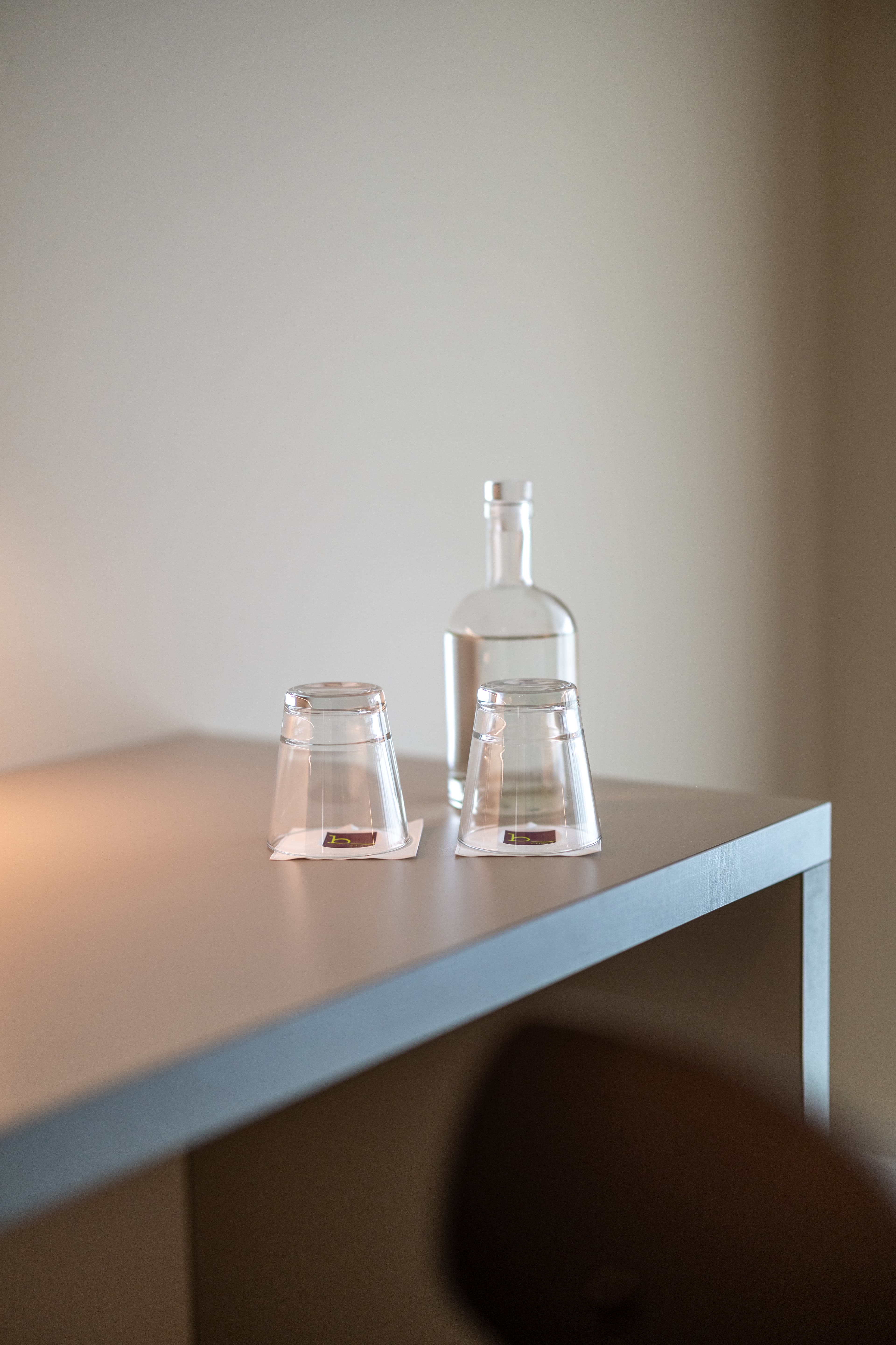 On a table in a B_smart motel room in Amriswil are a filled water carafe and two upside down glasses.