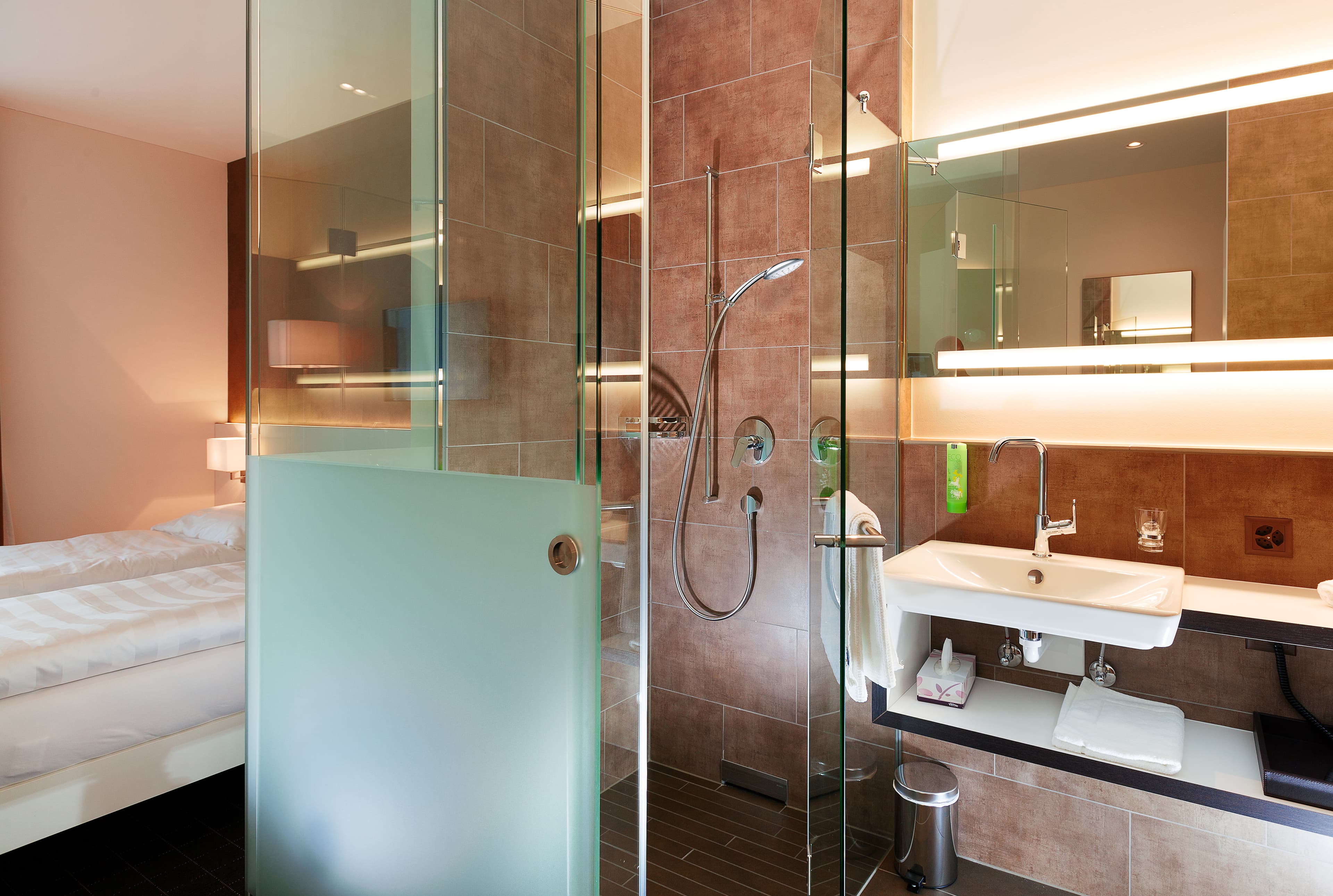 Modern well-lit double room at B Smart Motel Sevelen with a stylish bathroom with glass walls