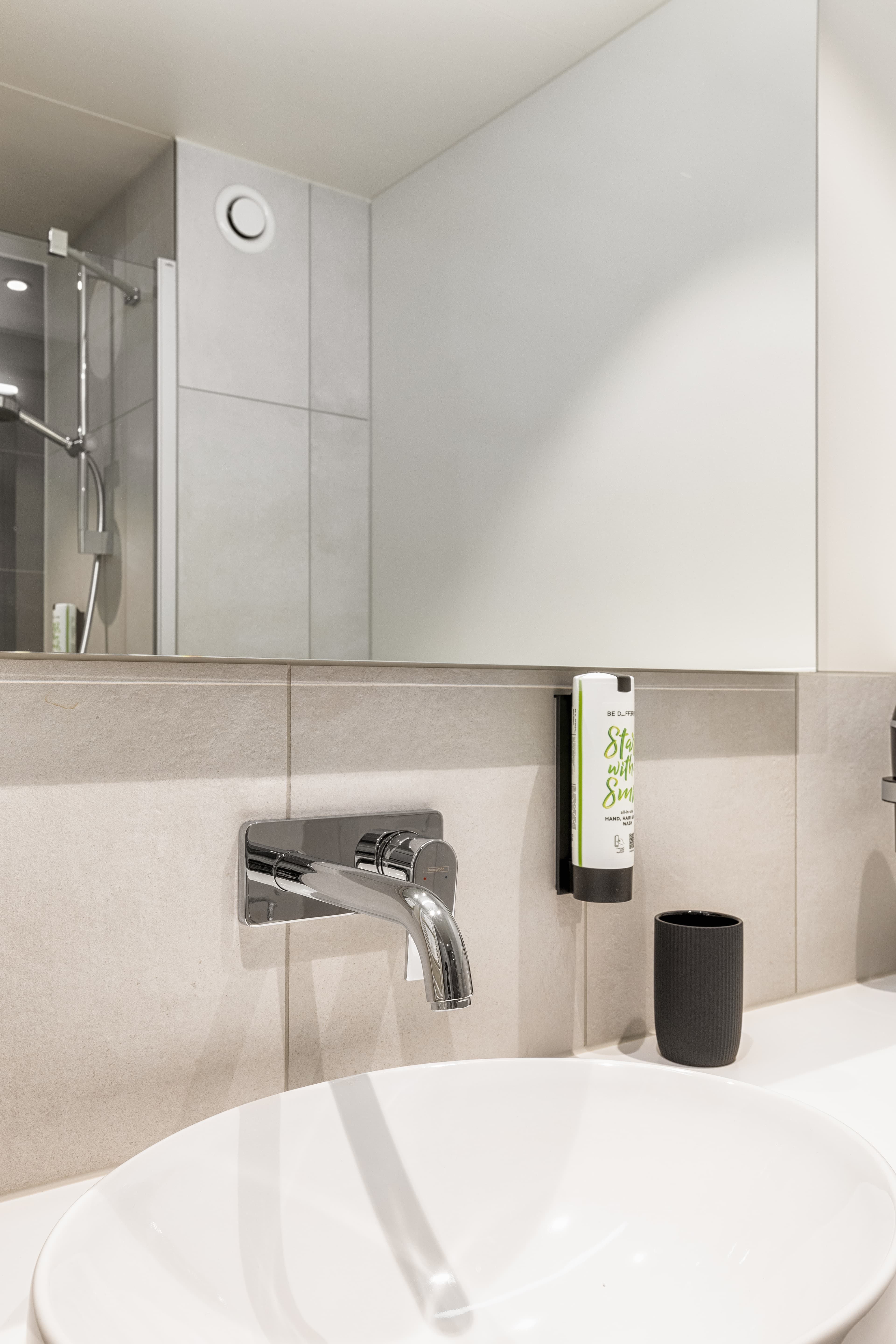 A modern bathroom in the B Smart Motel Amriswil with a white sink, chrome faucet, and soap dispenser on the wall