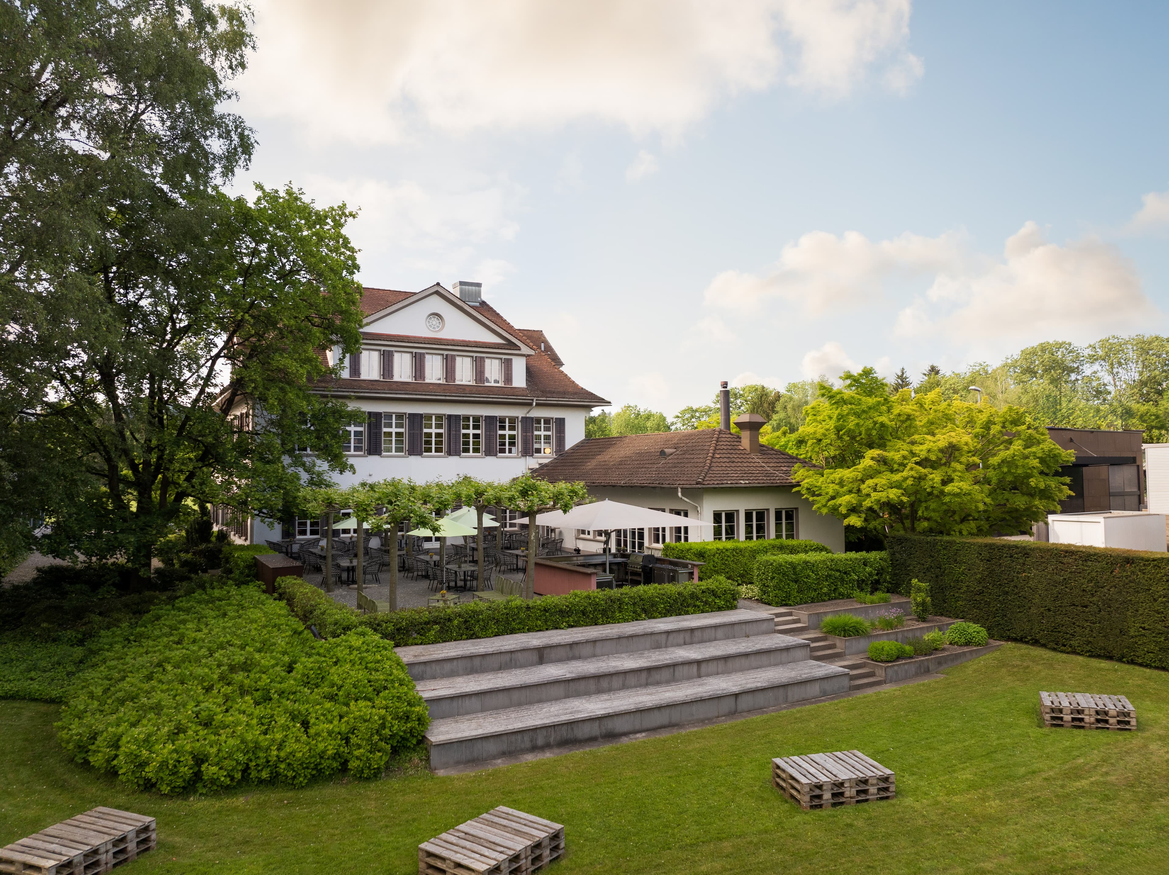 A modern hotel building with a large terrace and well-maintained garden at B Smart Hotel Widnau.