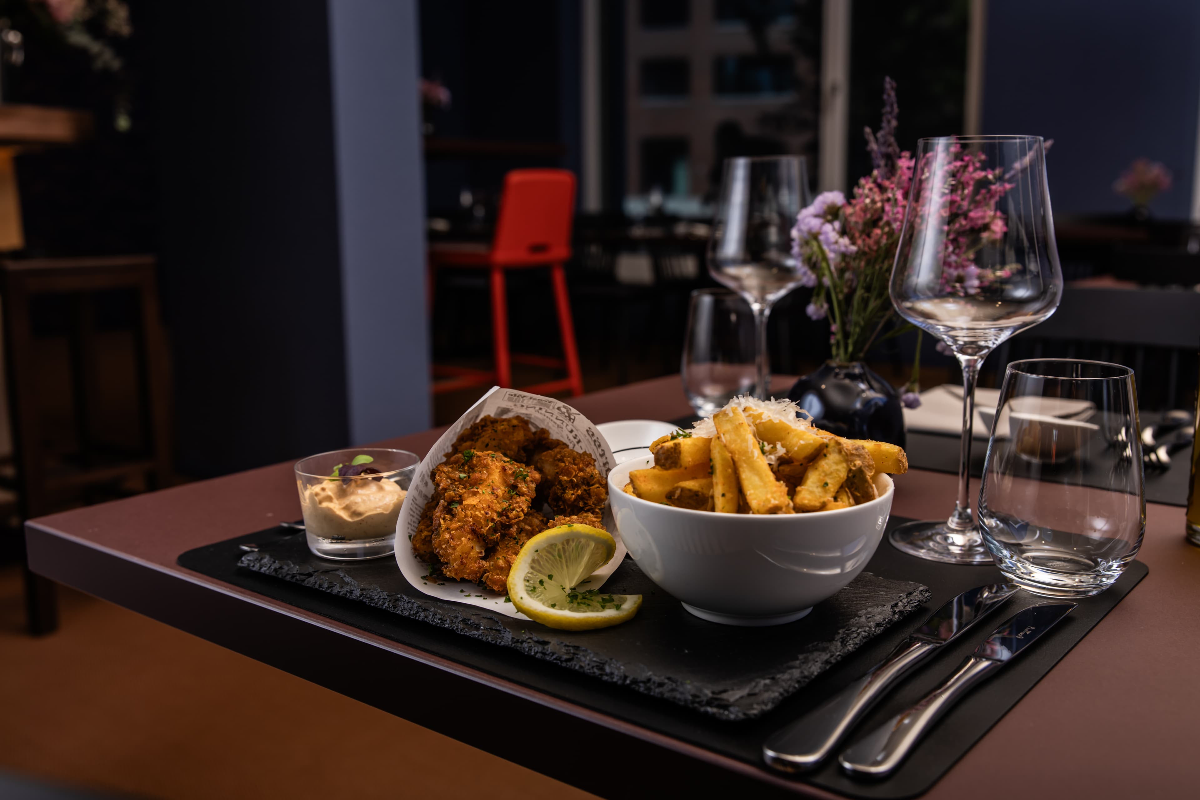 Table in an elegant restaurant with a plate of french fries, a glass of dipping sauce, and fried chicken decorated with lemon slices at the B Smart Hotel Arbon