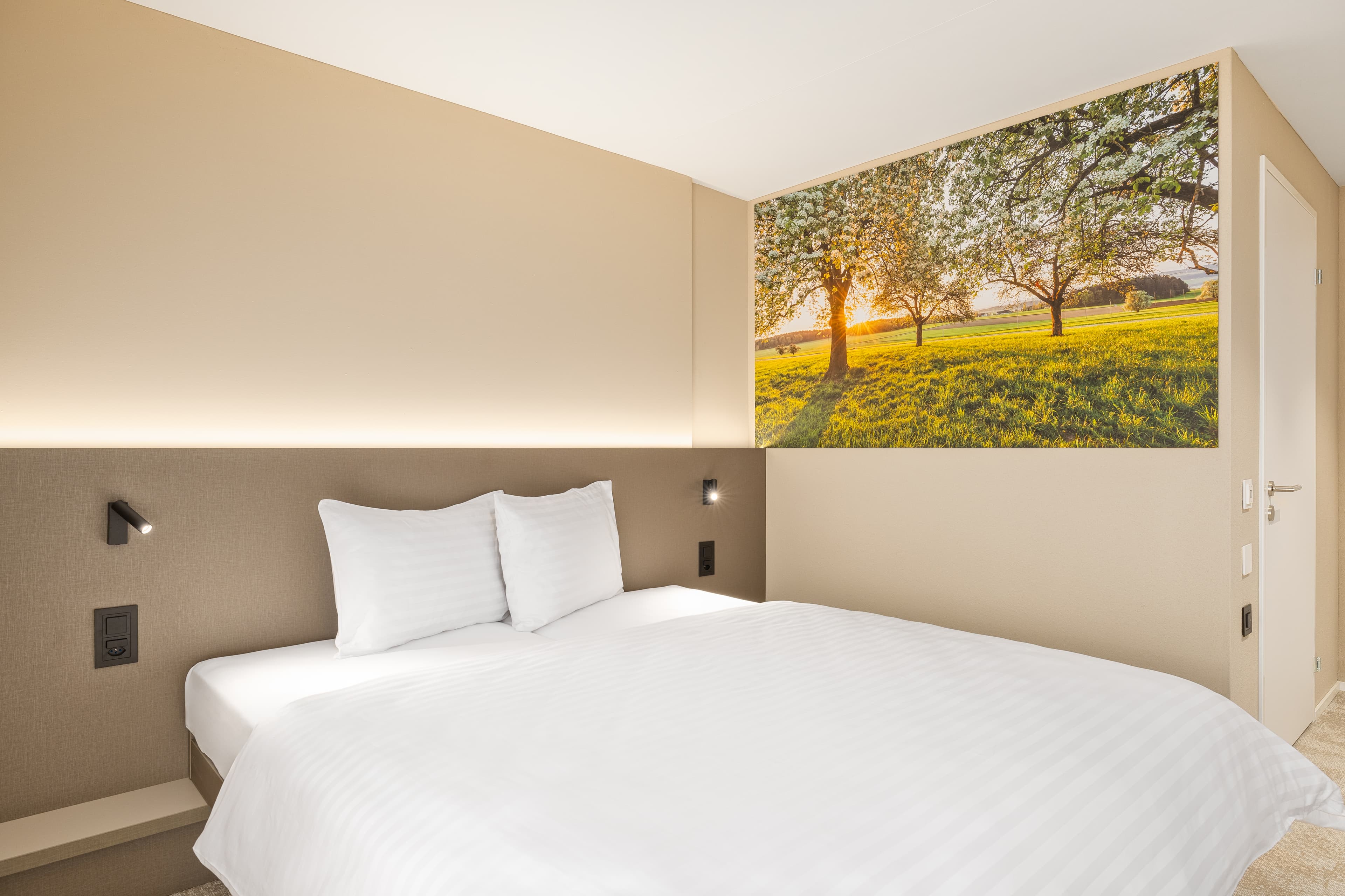 A double room in the Bsmart Motel Amriswil with a large bed and a wall decoration featuring a sunny landscape motif.