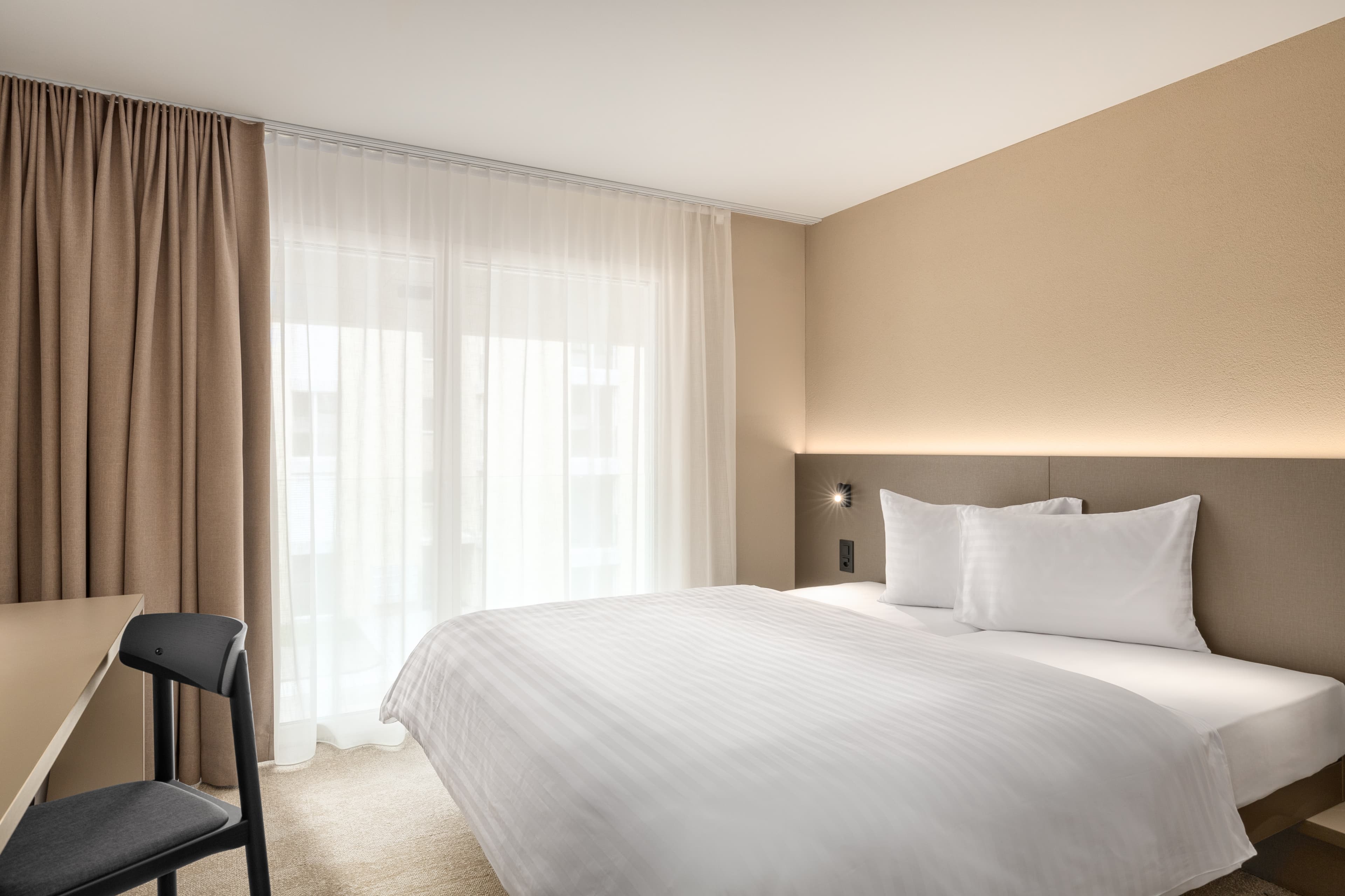 Standard double room at B Smart Motel Amriswil with a large bed bright curtains and a chair at a desk