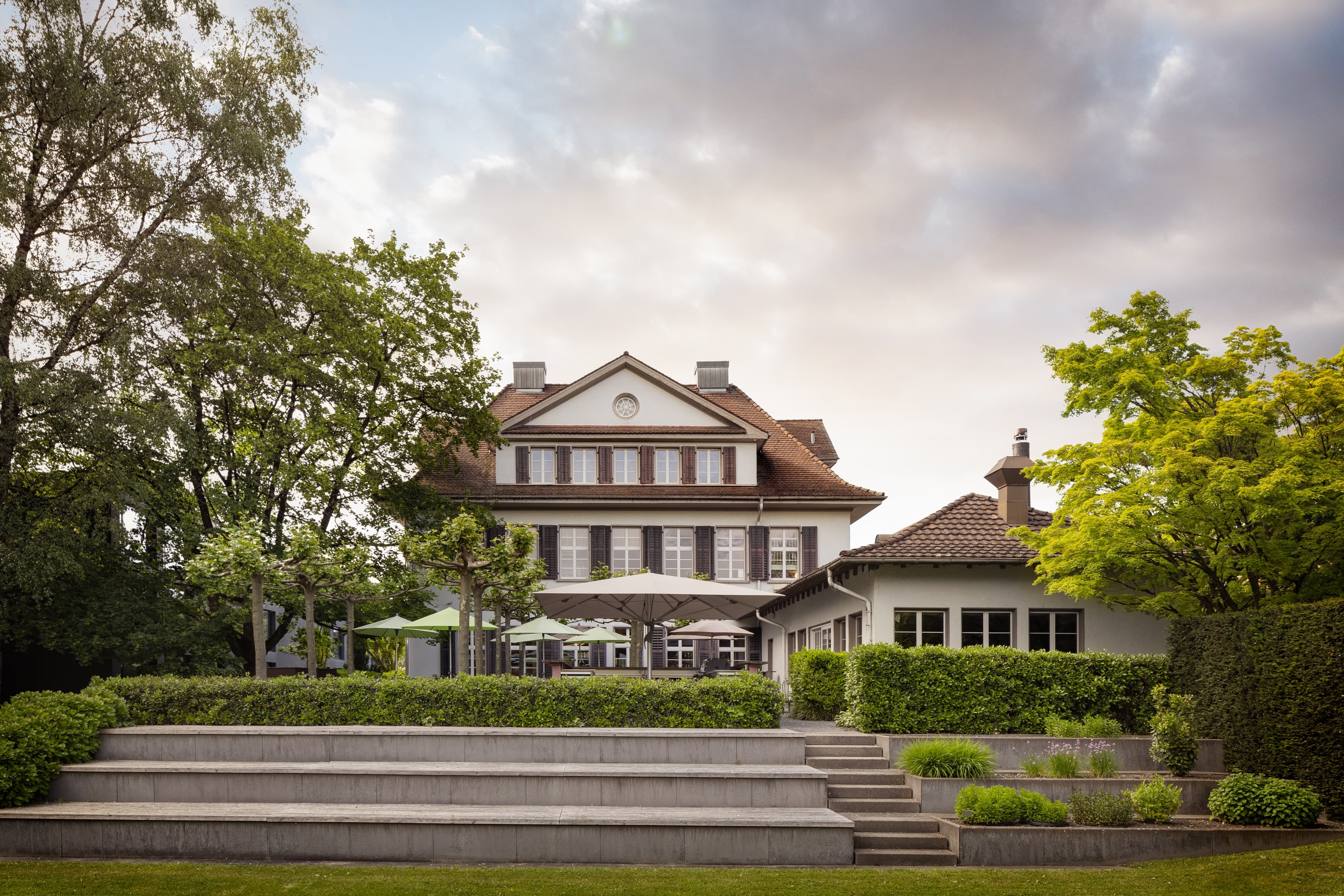 Exterior view of the B Smart Hotel in Widnau with a terrace-like park and lush greenery in the foreground