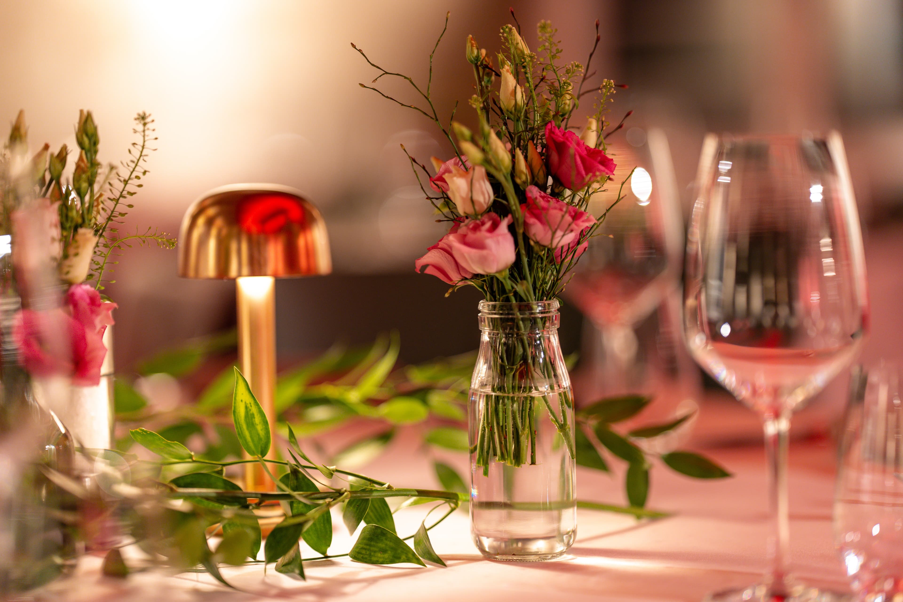 An elegant wedding table at the B_Smart Hotel Widnau with a vase of pink flowers surrounded by wine and water glasses and a table lamp