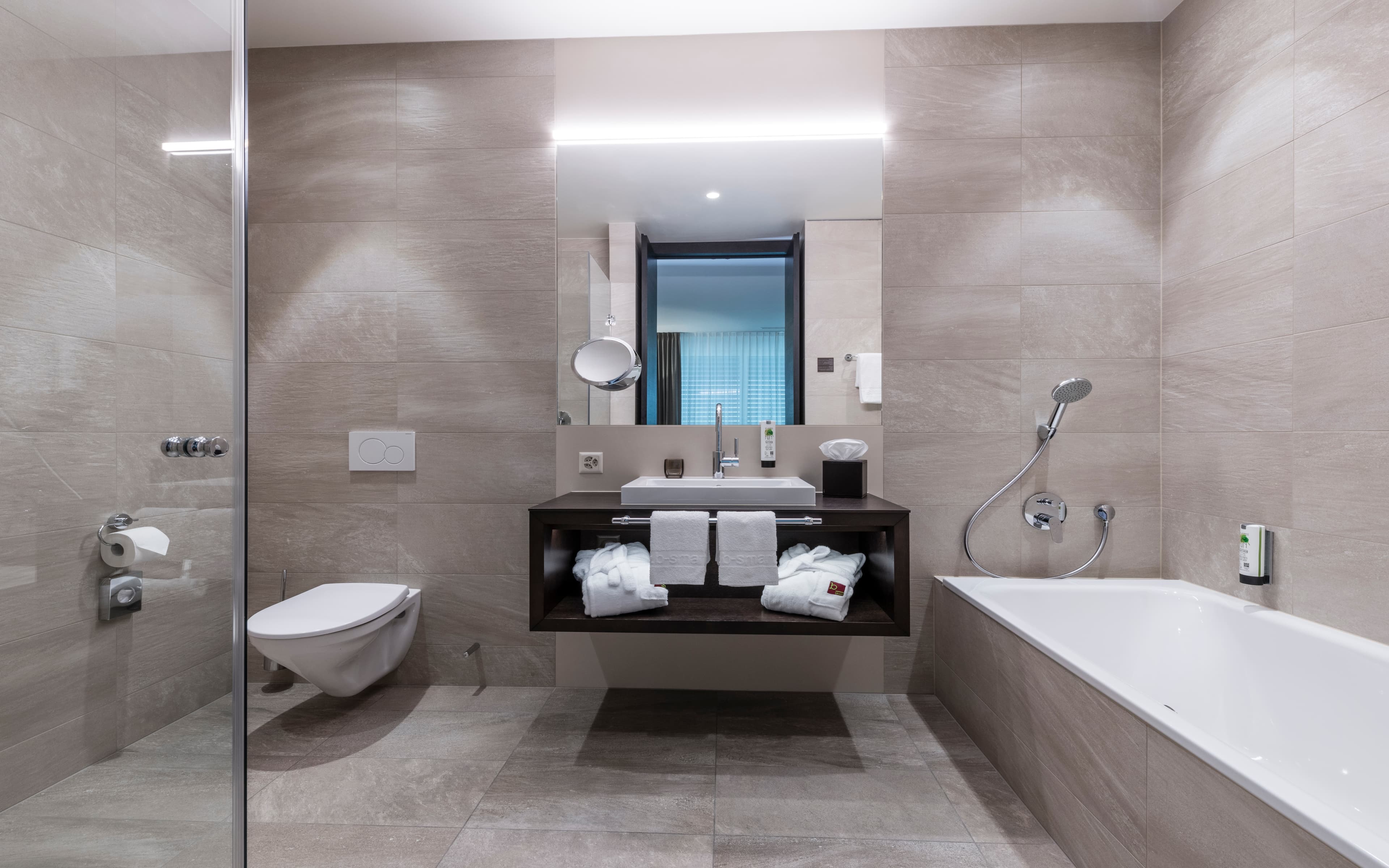 A modern bathroom in a Junior Suite at the B Smart Hotel Bendern with a bathtub, toilet, sink, and towels.
