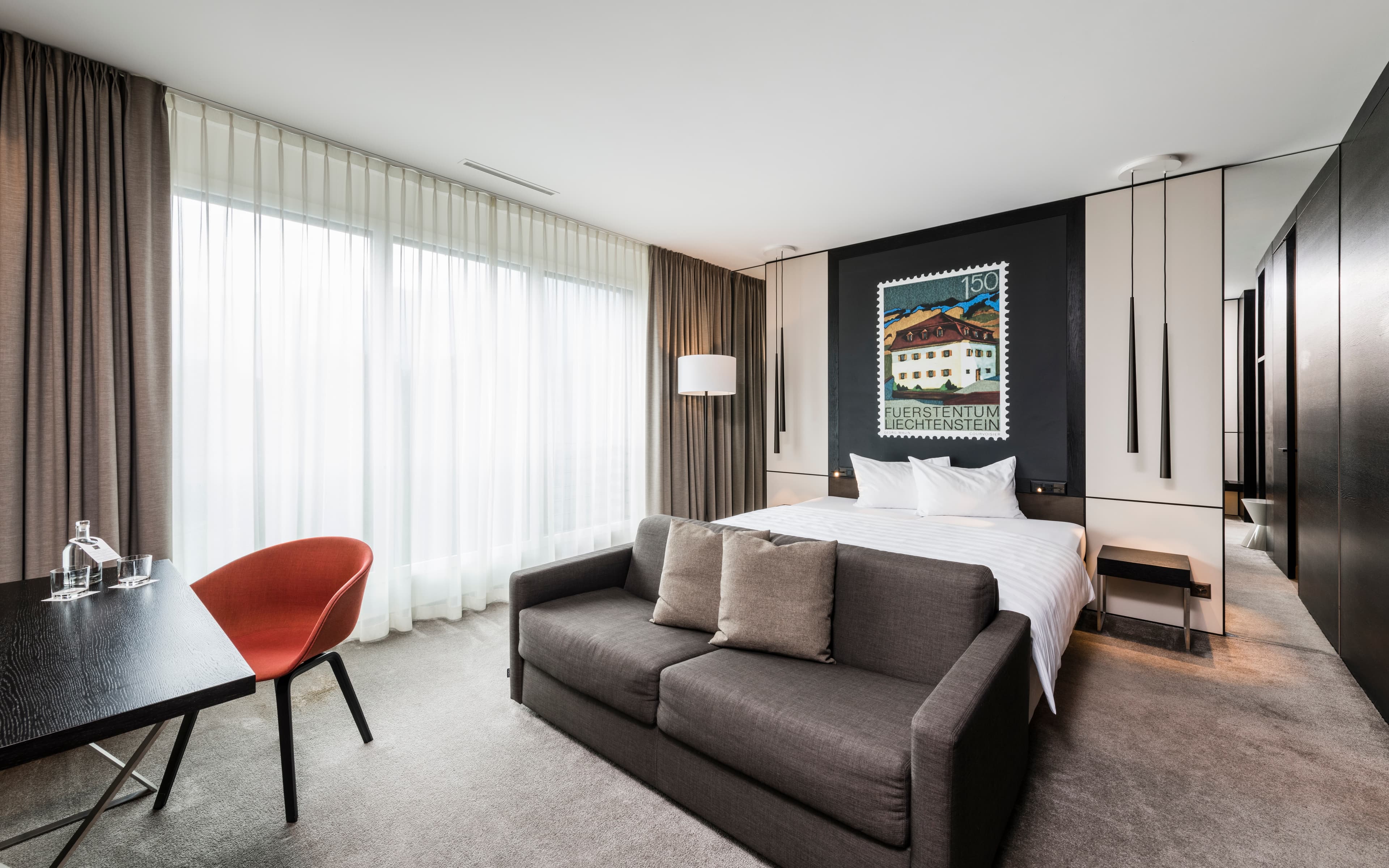 A Junior Suite Comfort at the B_smart Hotel Bendern with a bed, a sofa, a table with an orange chair, and bright, modern decor.