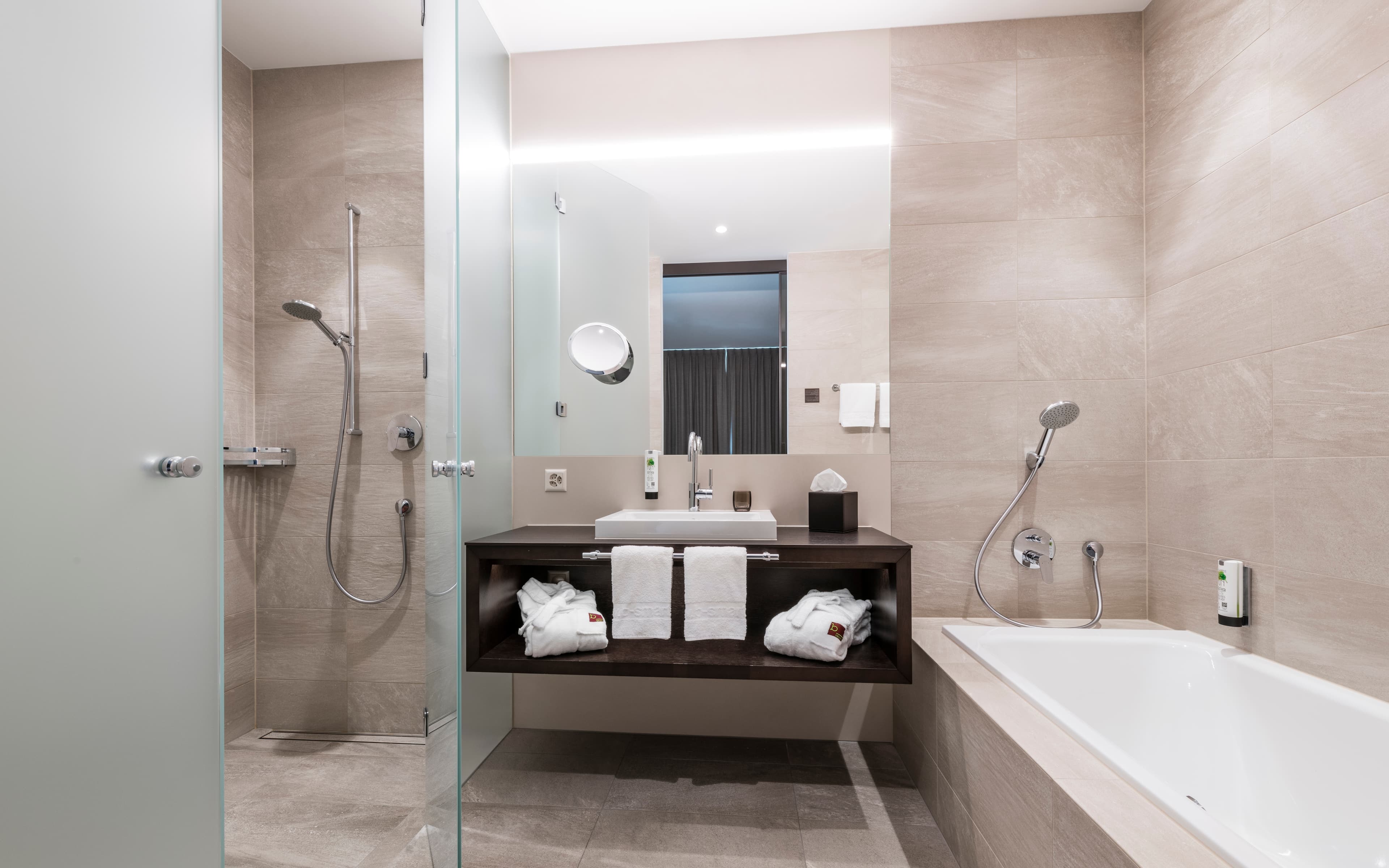 Modern bathroom of a Comfort Suite in the B_smart Hotel Bendern with glass shower cabin, sink, bathtub, and towels.
