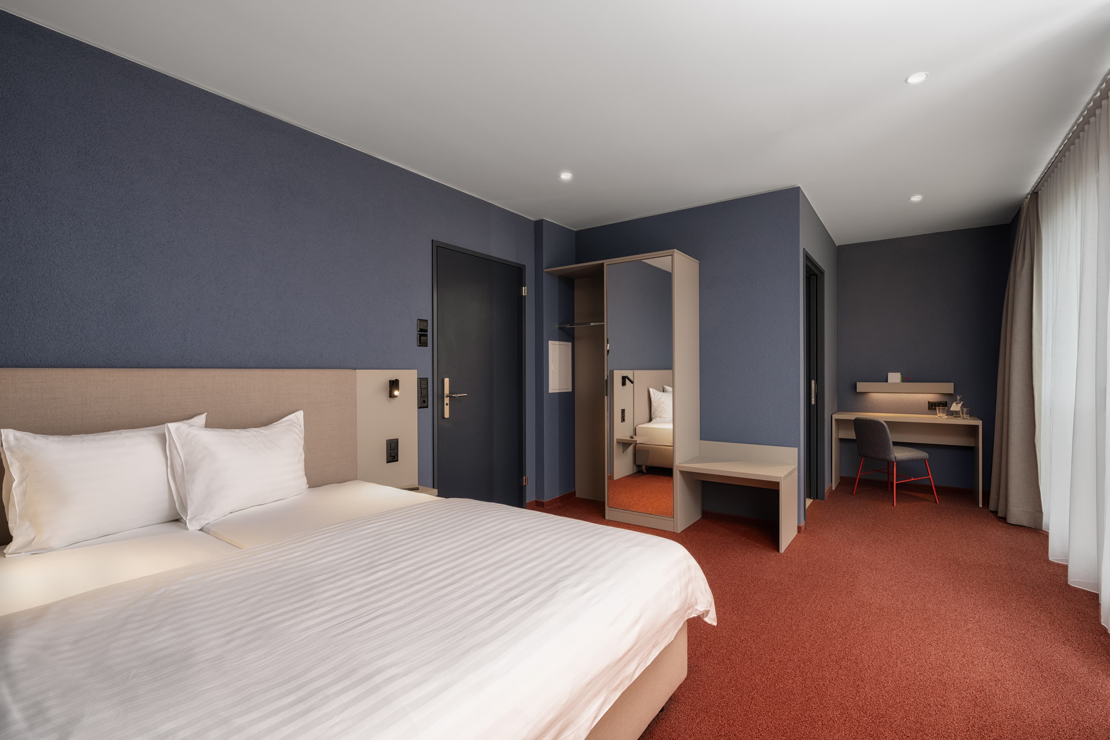 A modern, simply furnished Superior Double Room at the B Smart Hotel Arbon with a large bed, a desk, and a wardrobe.