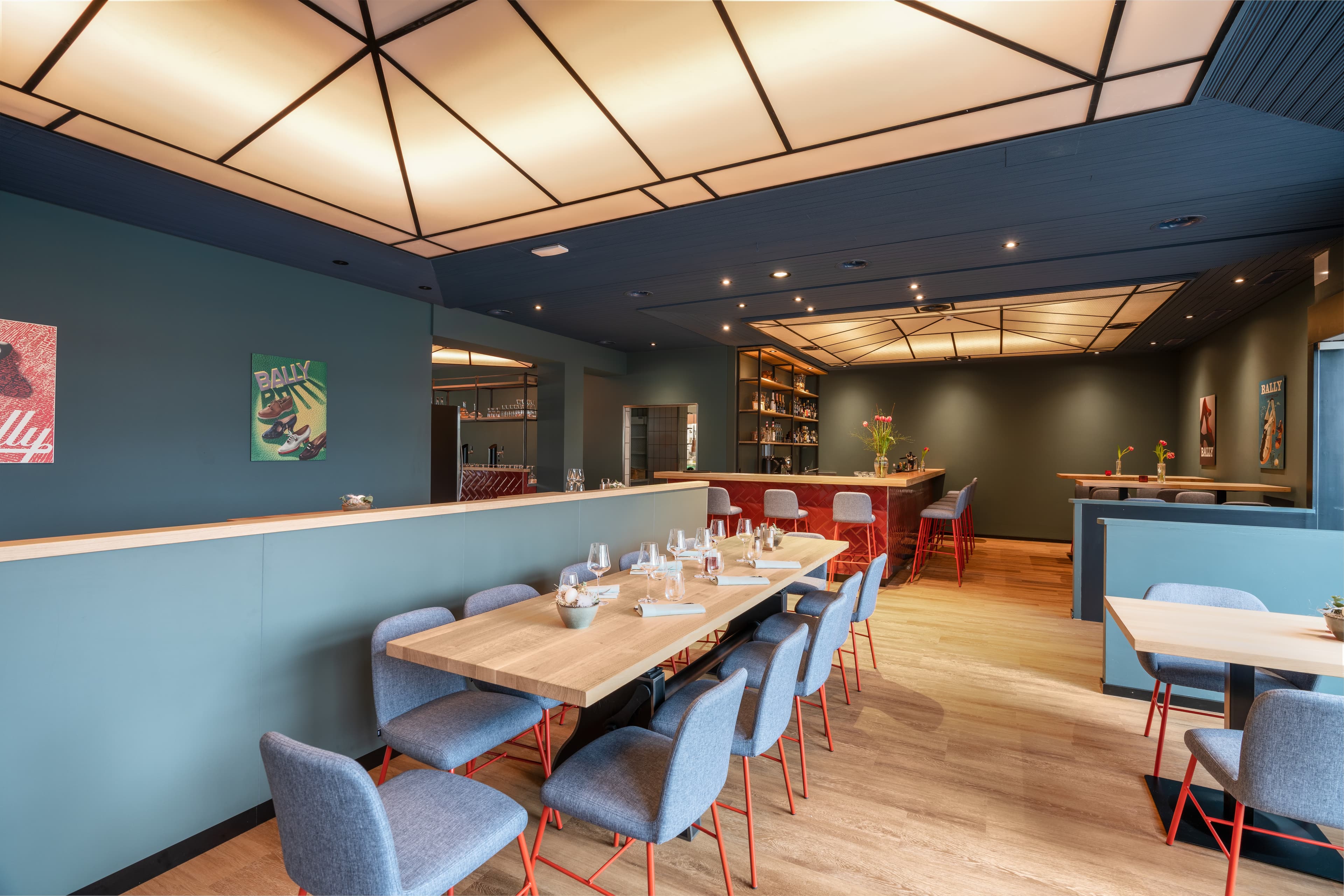 Modern dining room in the B Smart Hotel Schoenenwerd with light wooden tables gray chairs and a counter in the background decorated with flowers and stylish lighting elements